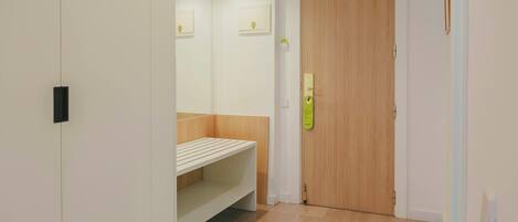 A hallway with a wooden door, a white bench, and a mirror on the wall.