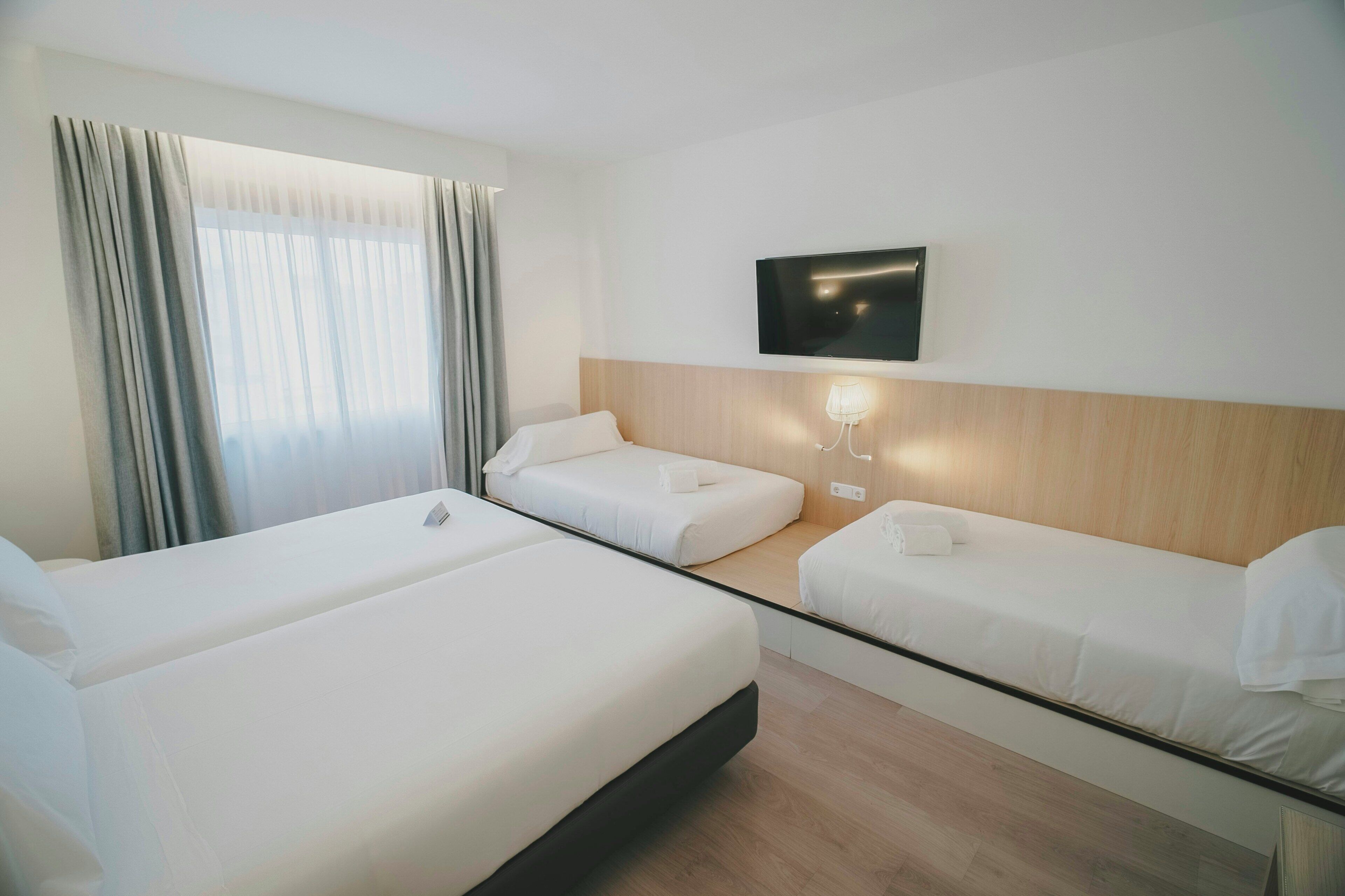 Een hotelkamer met twee bedden, een televisie en een raam met gordijnen.