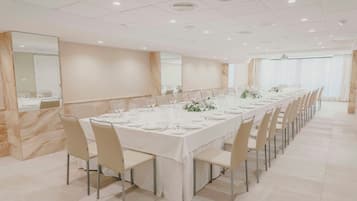Una larga mesa de comedor dispuesta con sillas, una pared de mármol y un amplio ventanal con cortinas.