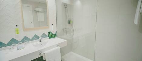 A modern bathroom with a glass-enclosed shower, a white sink with a mirror, and a green-tiled floor.