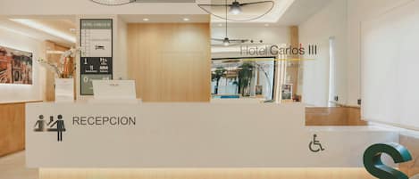 A hotel reception desk with a sign indicating 'Hotel Carlos III' and a 'Reception' sign.