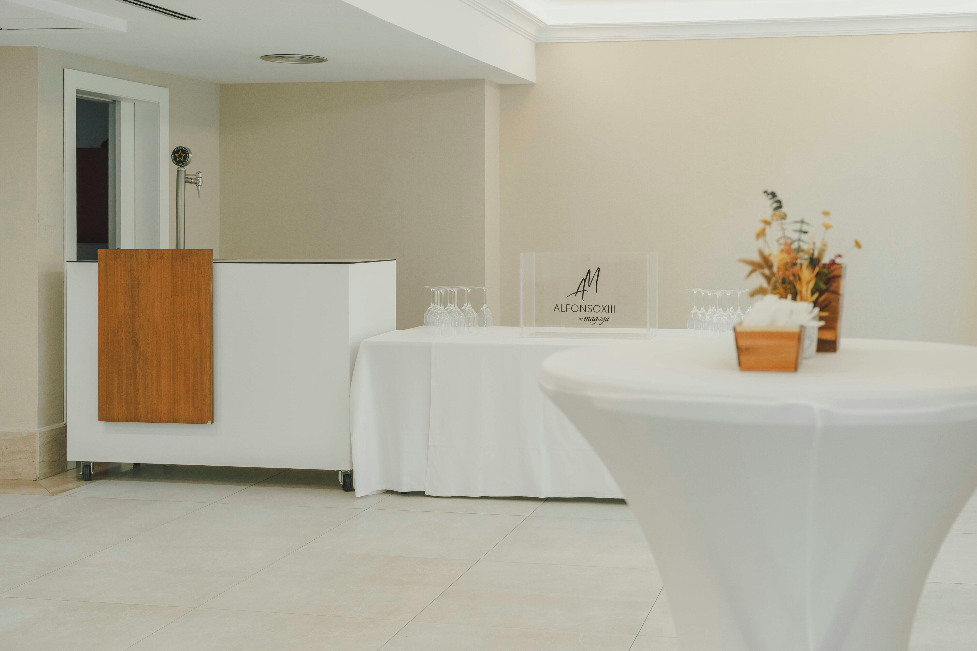 A reception area with a wooden panel, a white reception desk, a round table with a vase, and a wall-mounted sign.