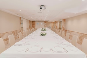 Sala de conferência com uma mesa comprida preparada para um evento formal, equipada com um projetor e um espelho grande na parede.