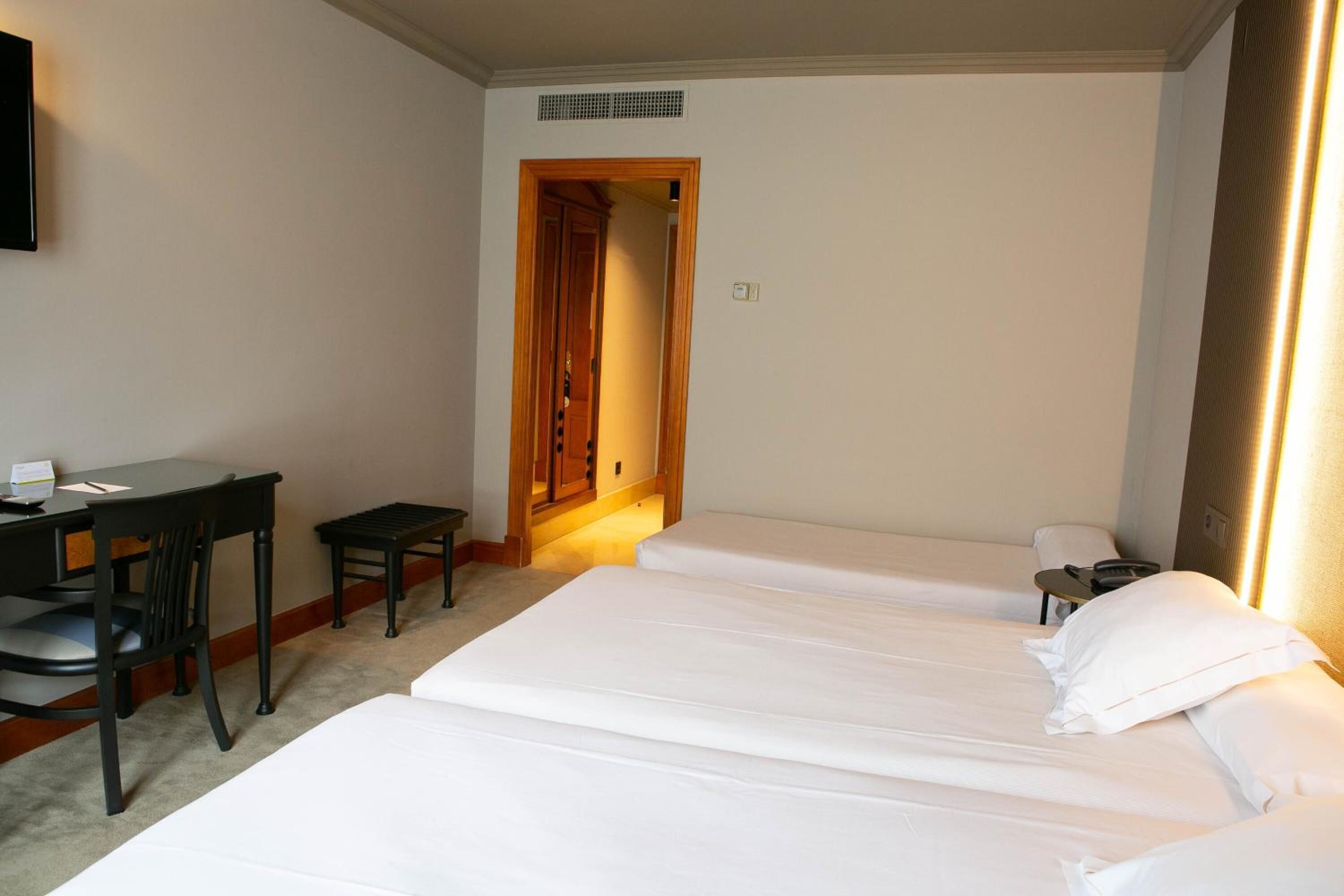 Una habitación de hotel con dos camas individuales, un escritorio con una silla y una mesita.