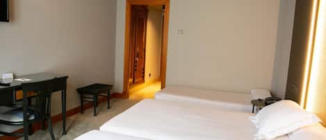 Una habitación de hotel con dos camas individuales, un escritorio con una silla y una mesita.