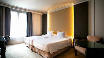 A hotel room with a large bed, a desk, a chair, and a small table.