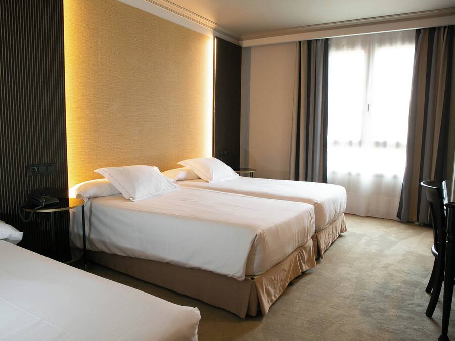 Une chambre d’hôtel avec deux lits, un bureau, une chaise et une grande fenêtre avec des rideaux.