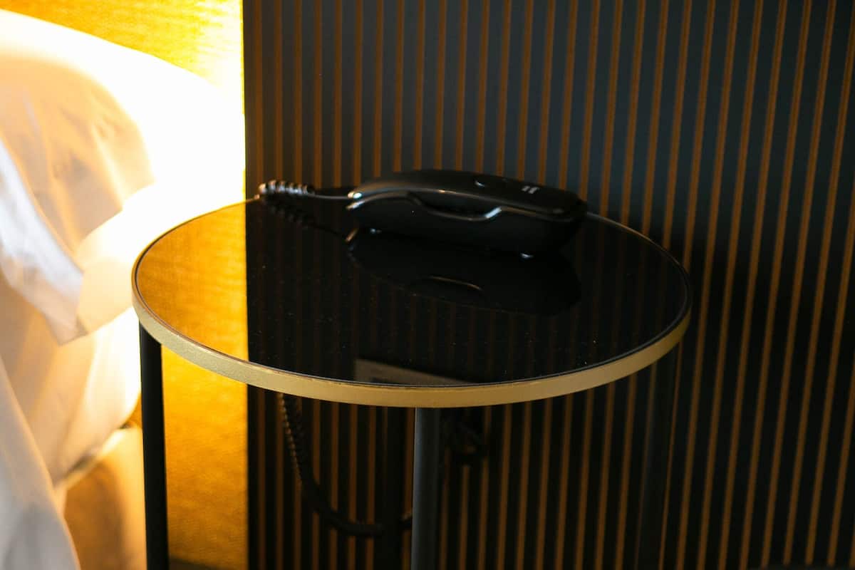 A small round table with a black telephone on it, a wicker chair, and a magazine on the table.