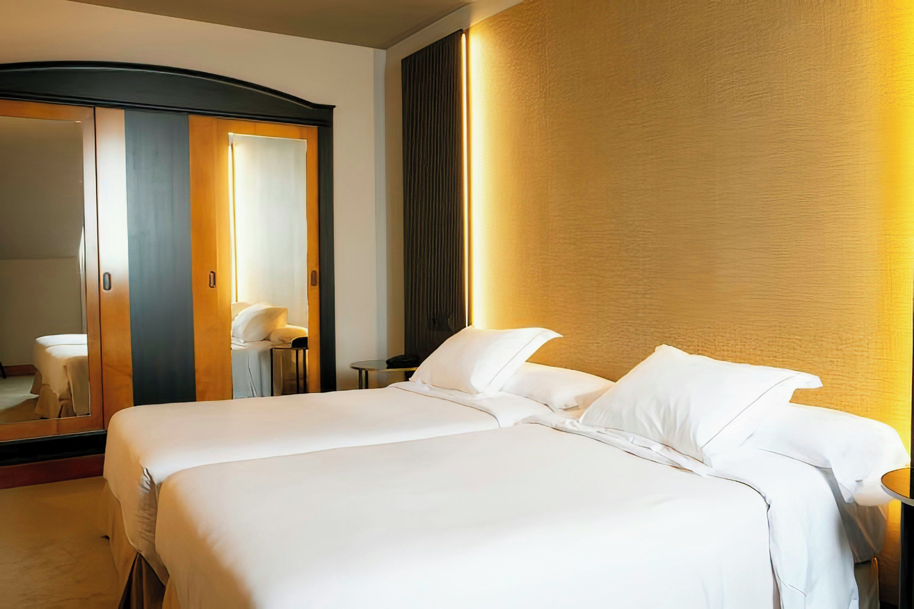 A hotel room with a large bed, a mirror, a wardrobe, and a bedside table.