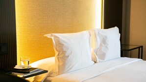 Una cama bien hecha con sábanas blancas, una mesita de noche con un vaso de agua y un libro, y una lámpara que emite una luz cálida.