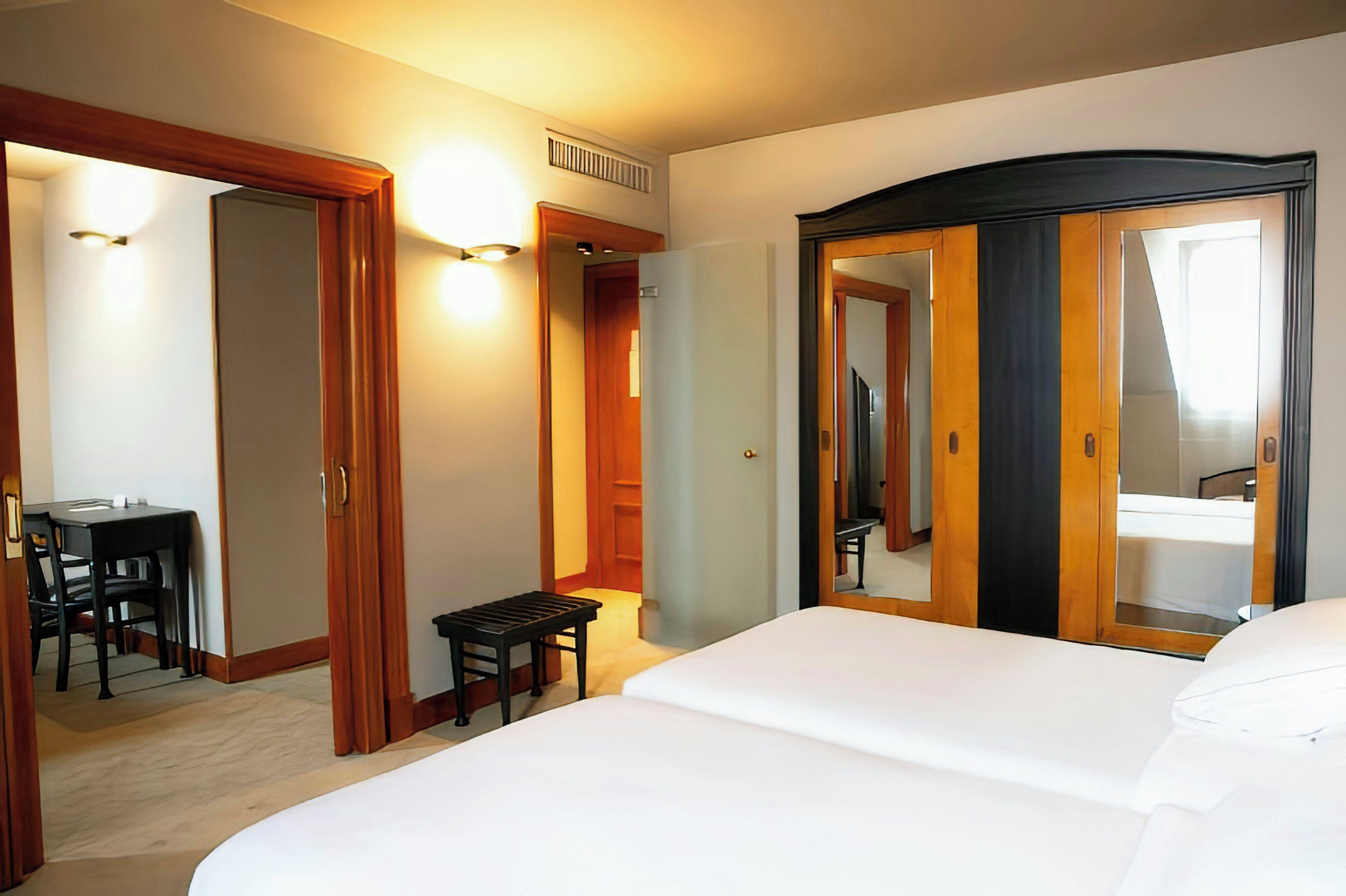 A hotel room with a bed, a desk, and a chair. There is a mirror and a wardrobe.