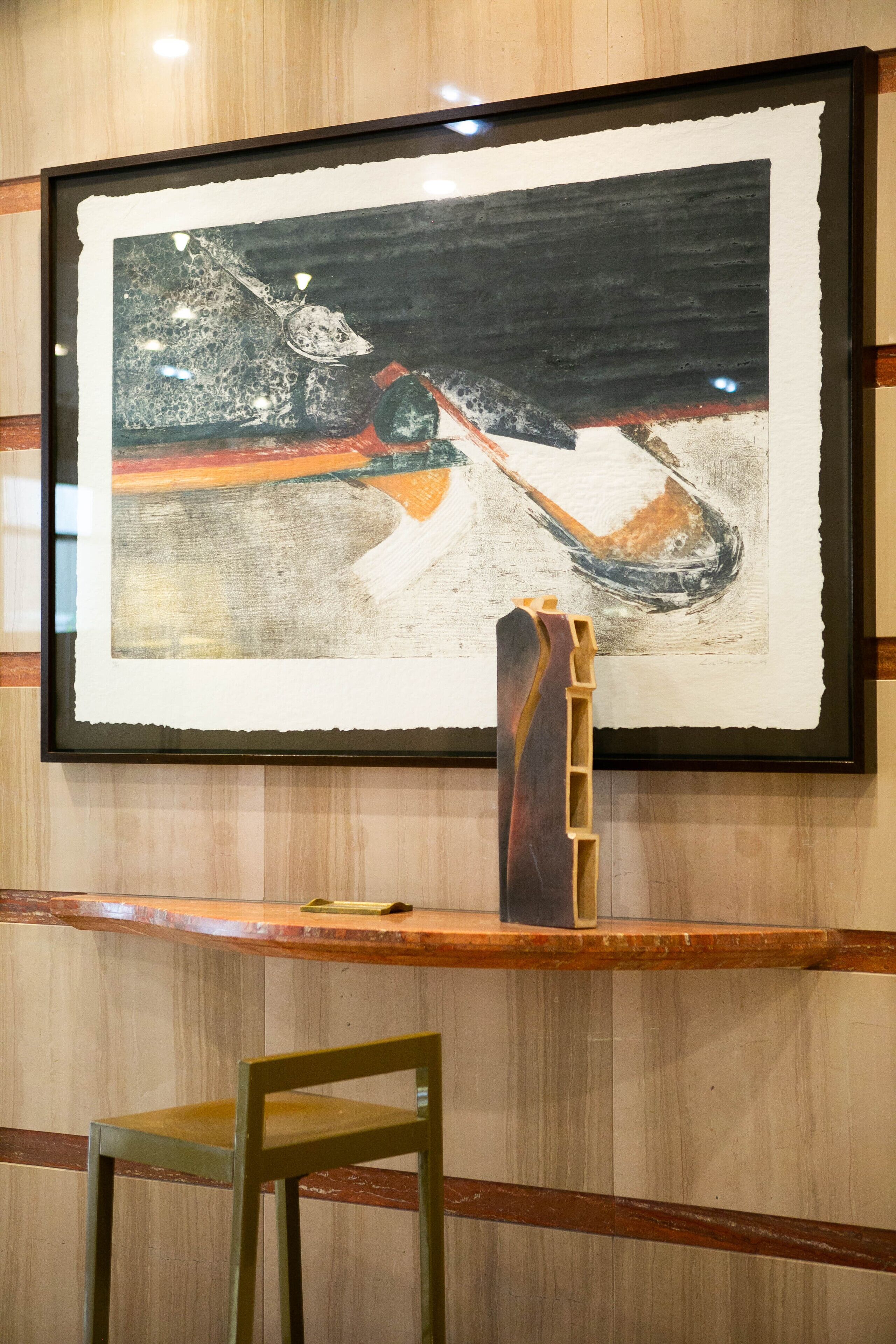 A framed artwork on a wall with a wooden chair in front.