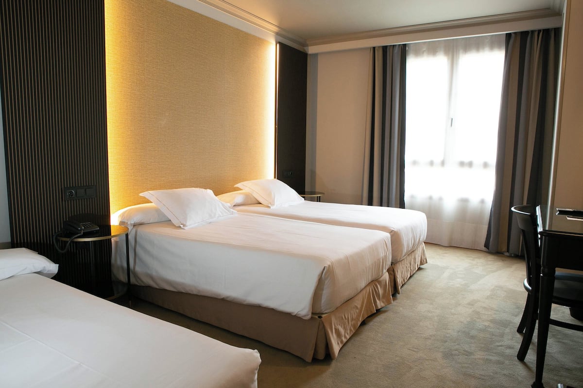 A hotel room with two beds, a desk, a chair, and a large window with curtains.