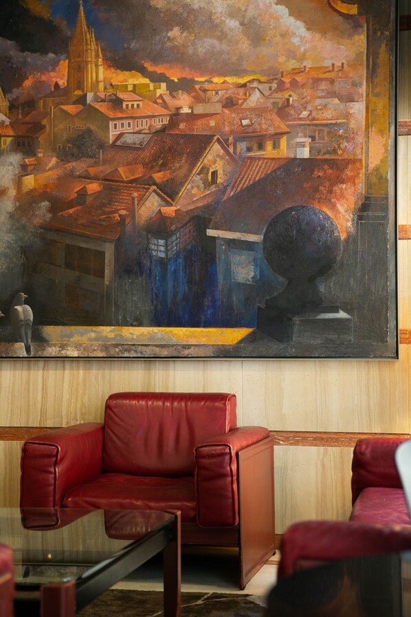 Una habitación con un cuadro grande de un paisaje urbano, un sofá de cuero rojo y una mesa de centro de vidrio.