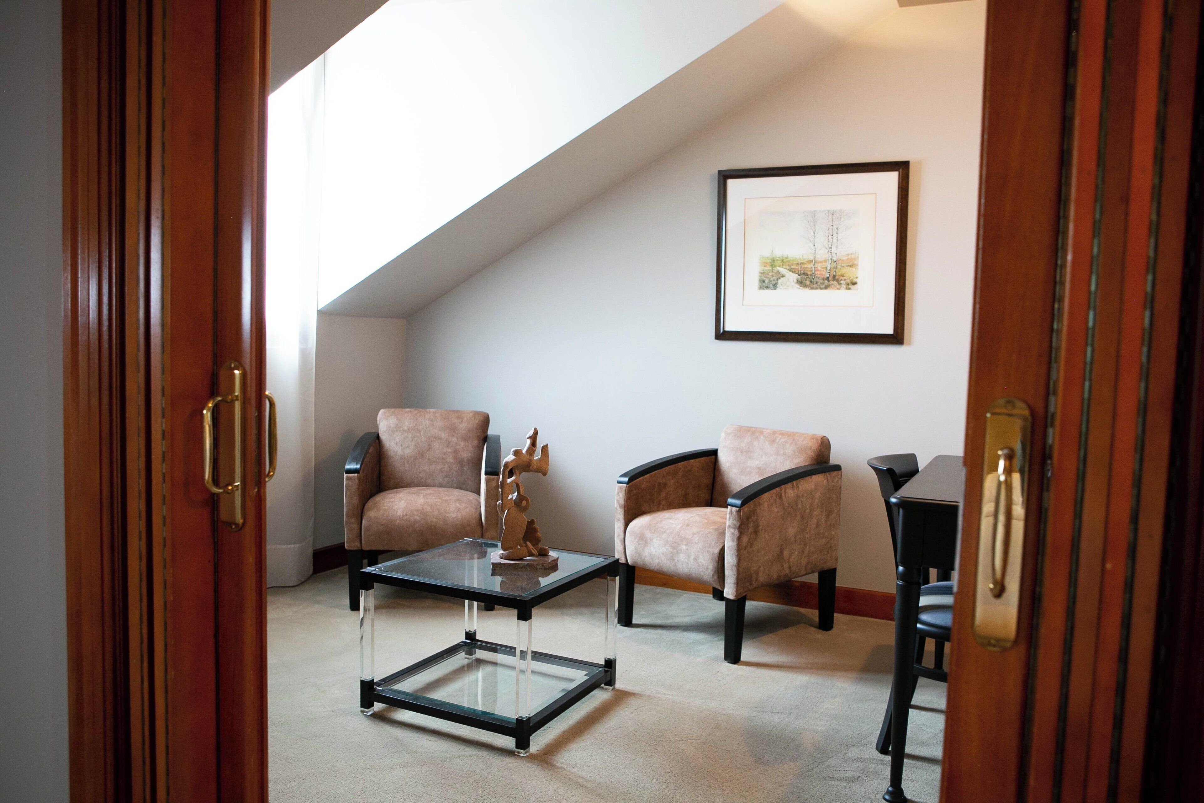Una habitación con dos sillones, una mesa de centro de vidrio y un cuadro en la pared.