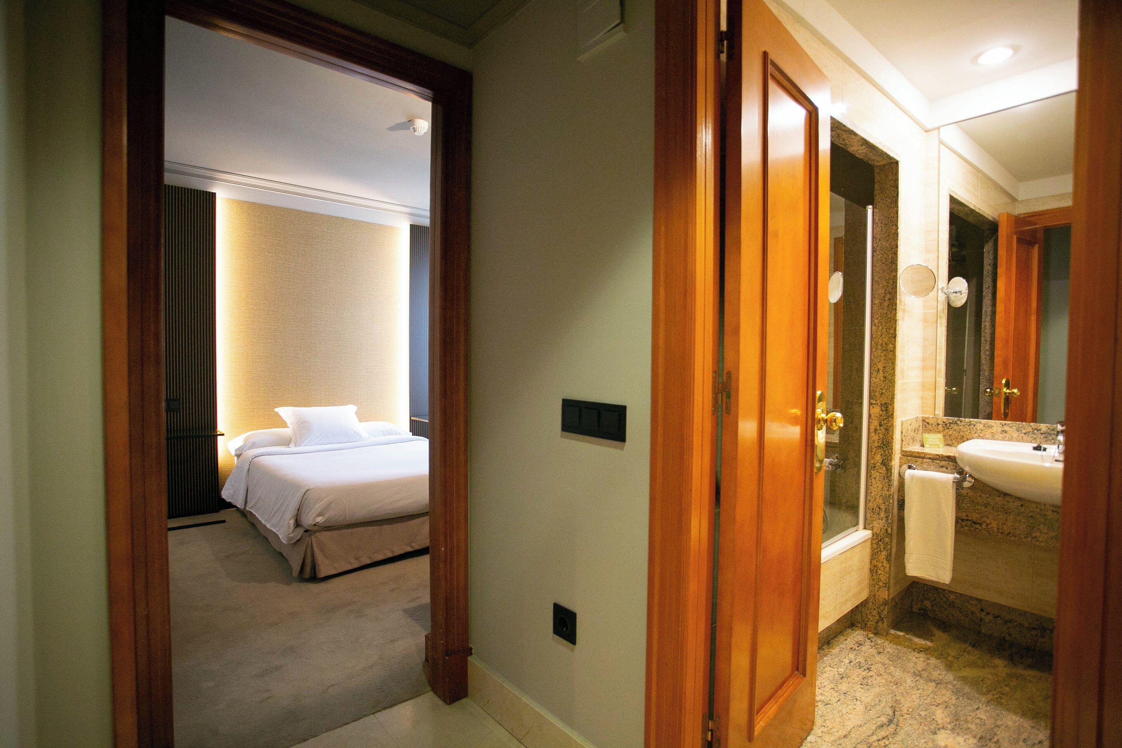 Una habitación de hotel con una cama, un baño con lavamanos y espejo, y una ducha.