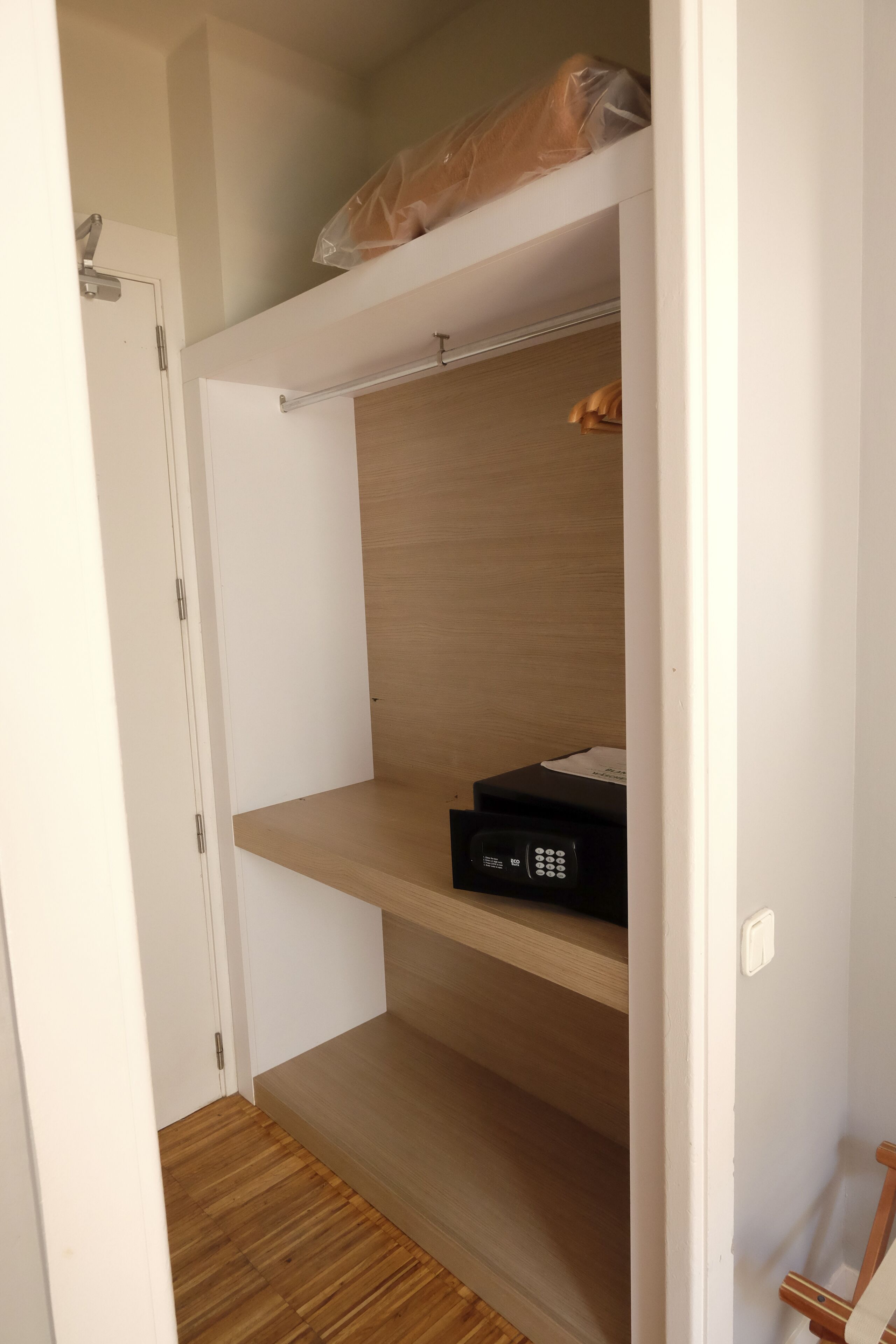 Une pièce avec un plancher en bois, des murs blancs et une porte blanche. On y trouve une étagère sur laquelle repose un objet noir.