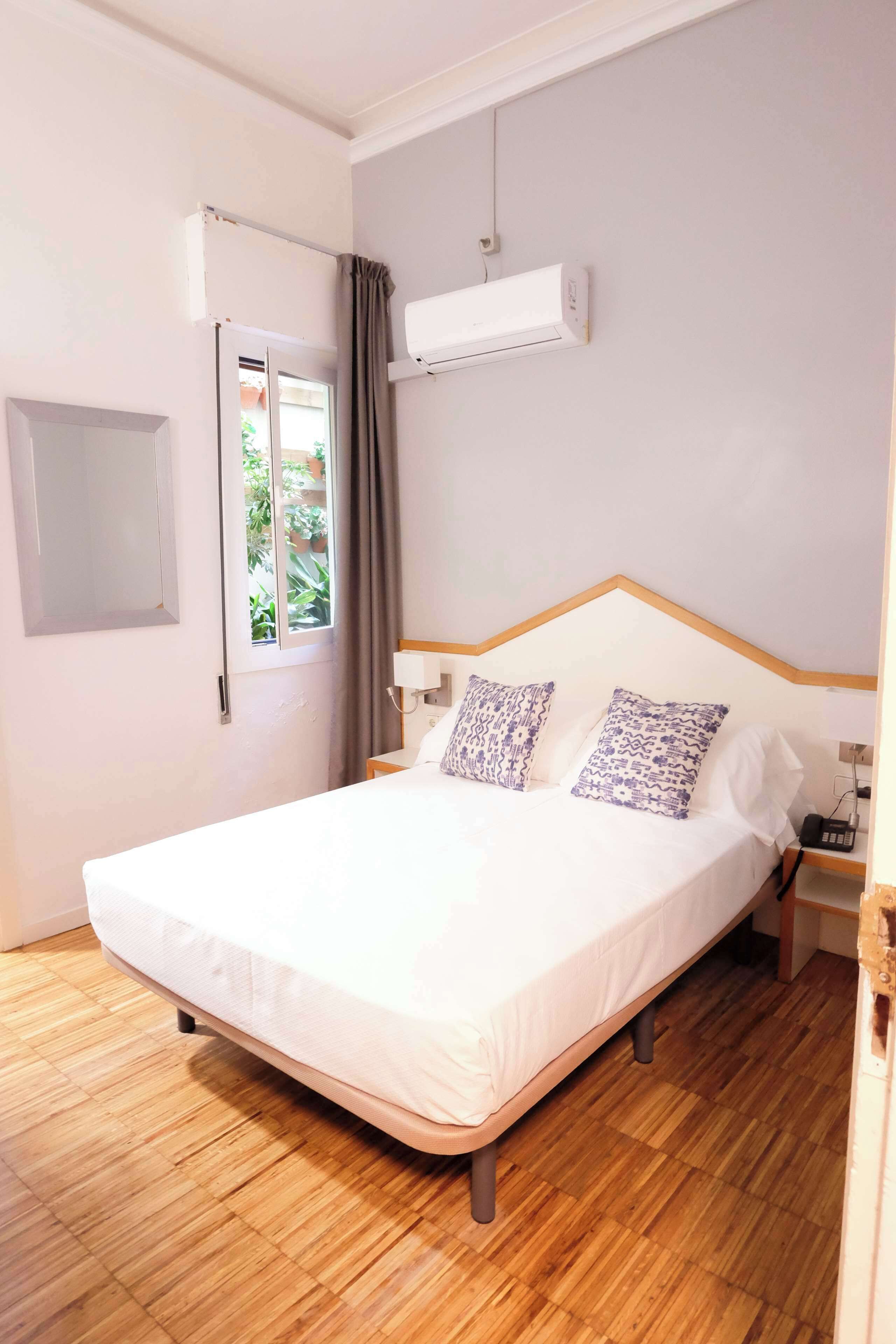 Een slaapkamer met een bed, een airconditioner, een nachtkastje en een raam met gordijnen.