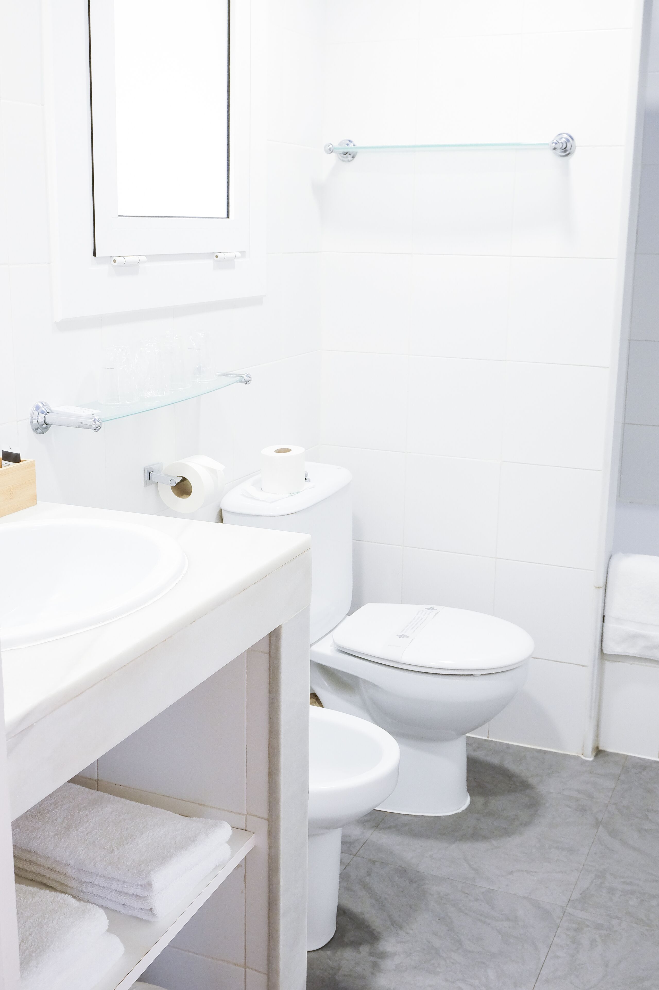 A bathroom with a white sink, two toilets, a glass shower enclosure, and a towel rack.