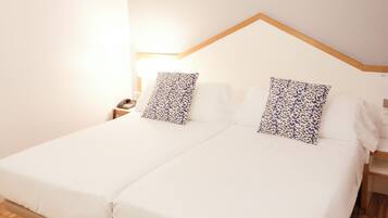 Una cama doble con ropa blanca, un cabecero de madera y dos mesitas de noche con lámparas.