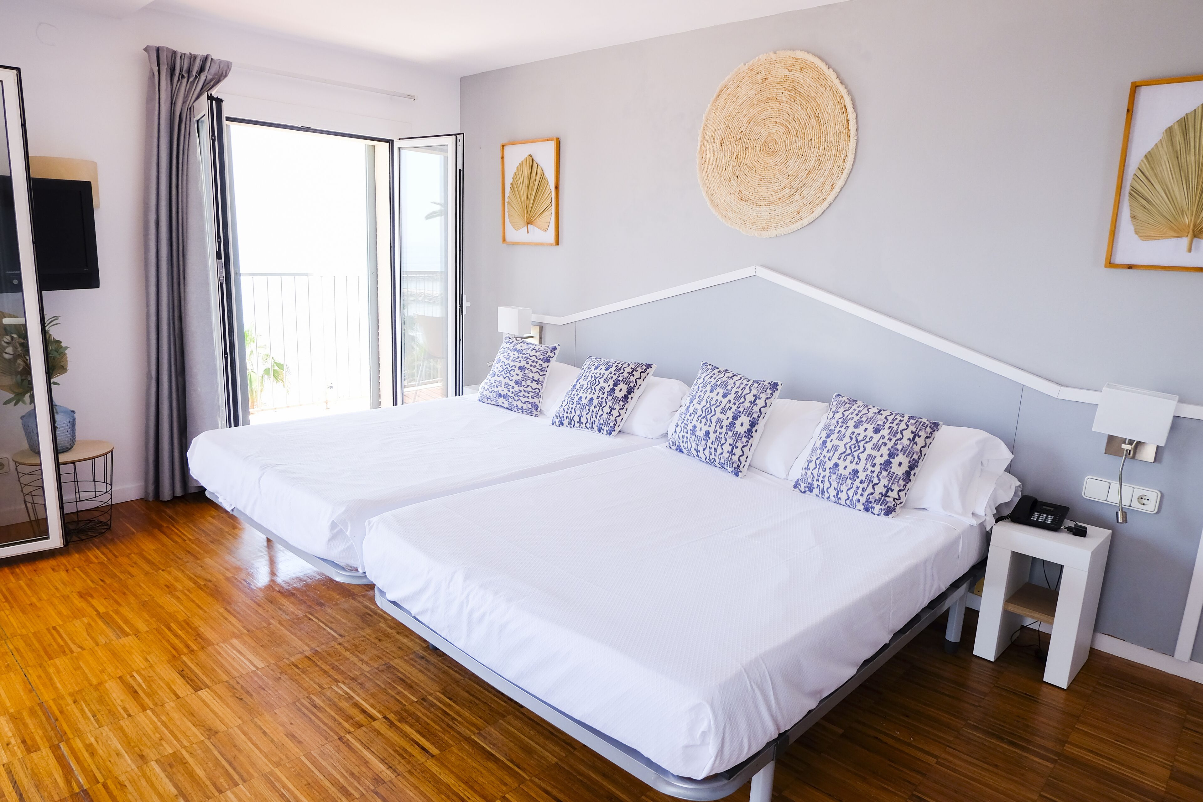 A double bed with white and blue patterned pillows, a bedside table with a phone, and a wall-mounted fan.