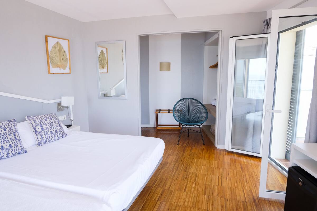 A bedroom with a large bed, a chair, a wardrobe, and a door leading to a balcony.