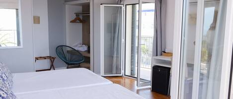 A modern bedroom with a large bed, a chair, a desk, and a sliding glass door leading to a balcony.