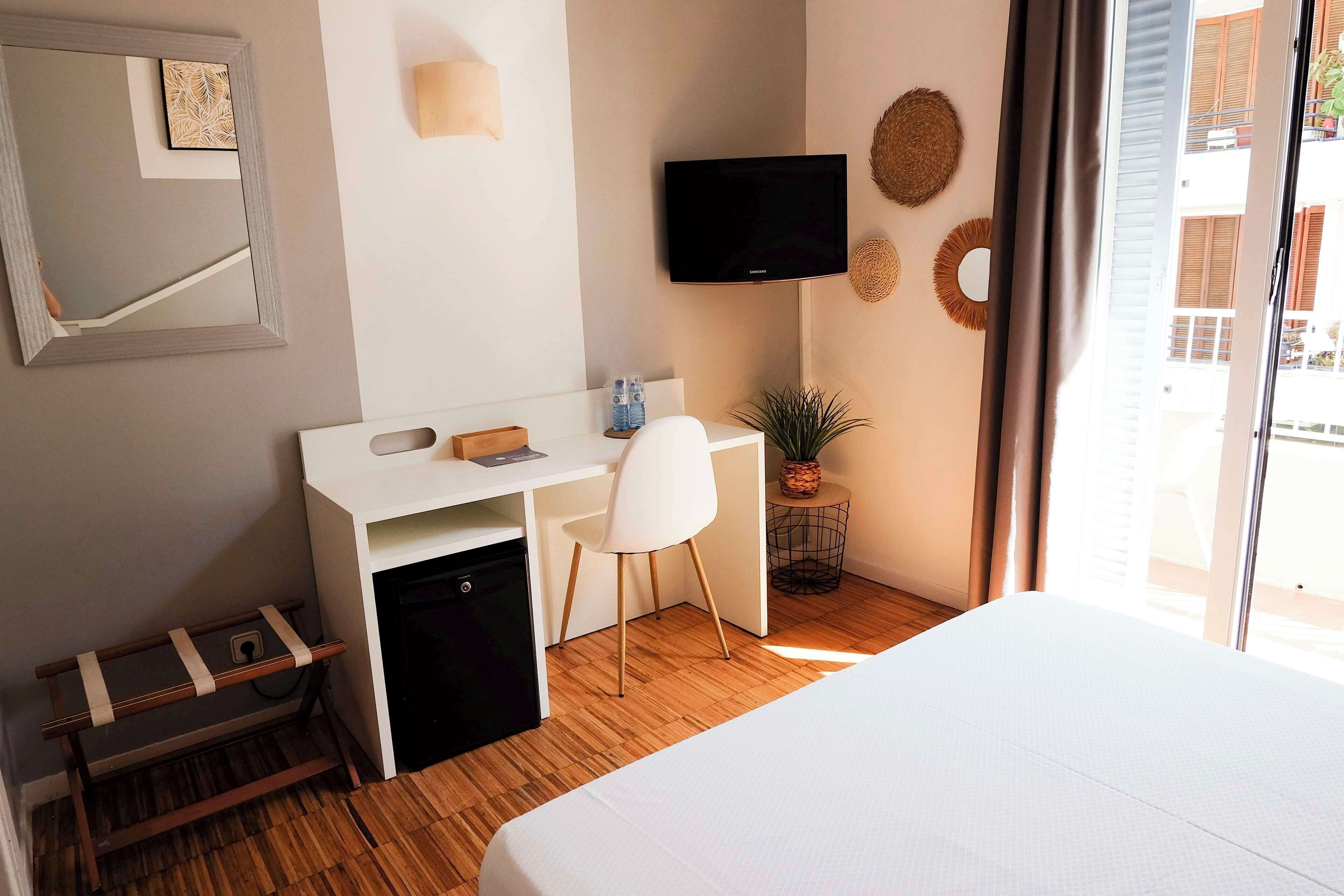 A hotel room with a bed, a desk with a chair, a television, and a window with curtains.