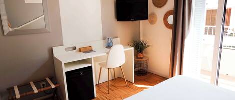 A hotel room with a bed, a desk with a chair, a television, and a window with curtains.
