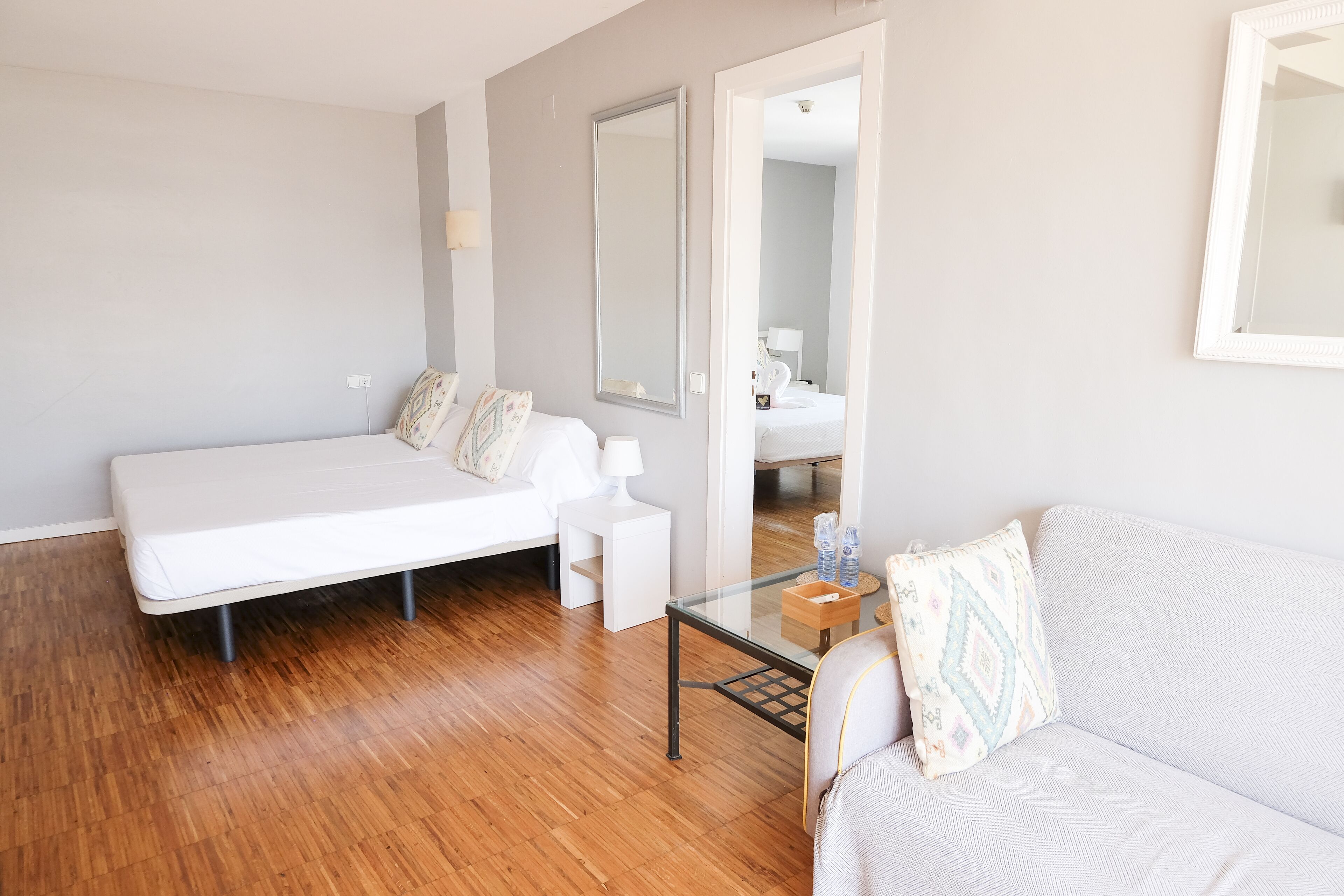 A modern, minimalist room with a bed, a sofa, a small table, and a mirror.