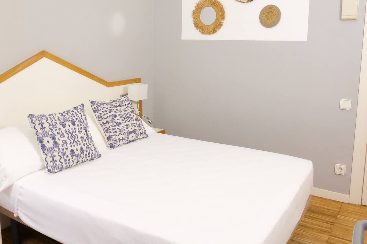 A bedroom with a bed, two patterned pillows, a bedside lamp, and wall art.