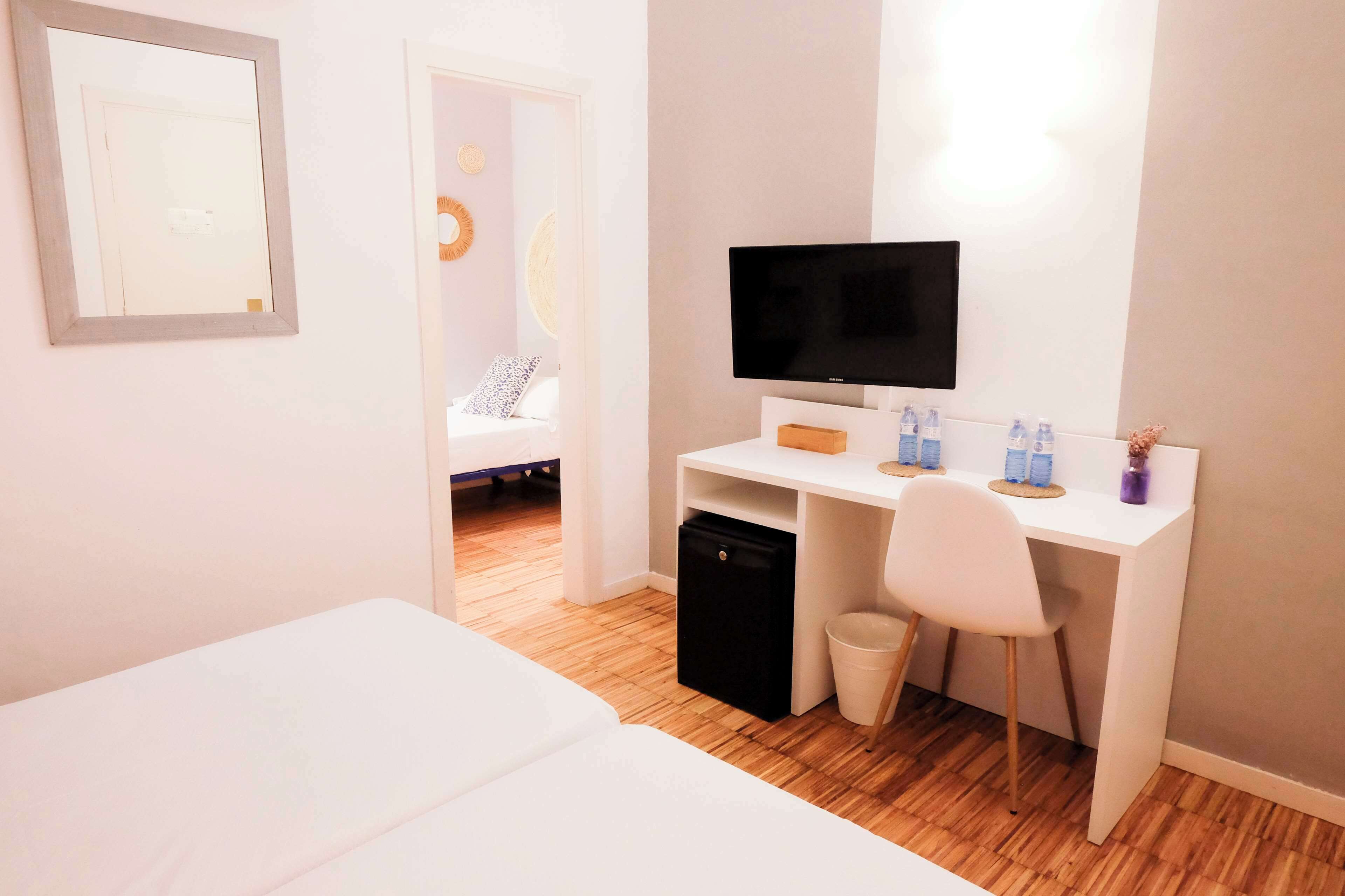 A modern hotel room with a white bed, a desk with a TV, and a small trash bin.