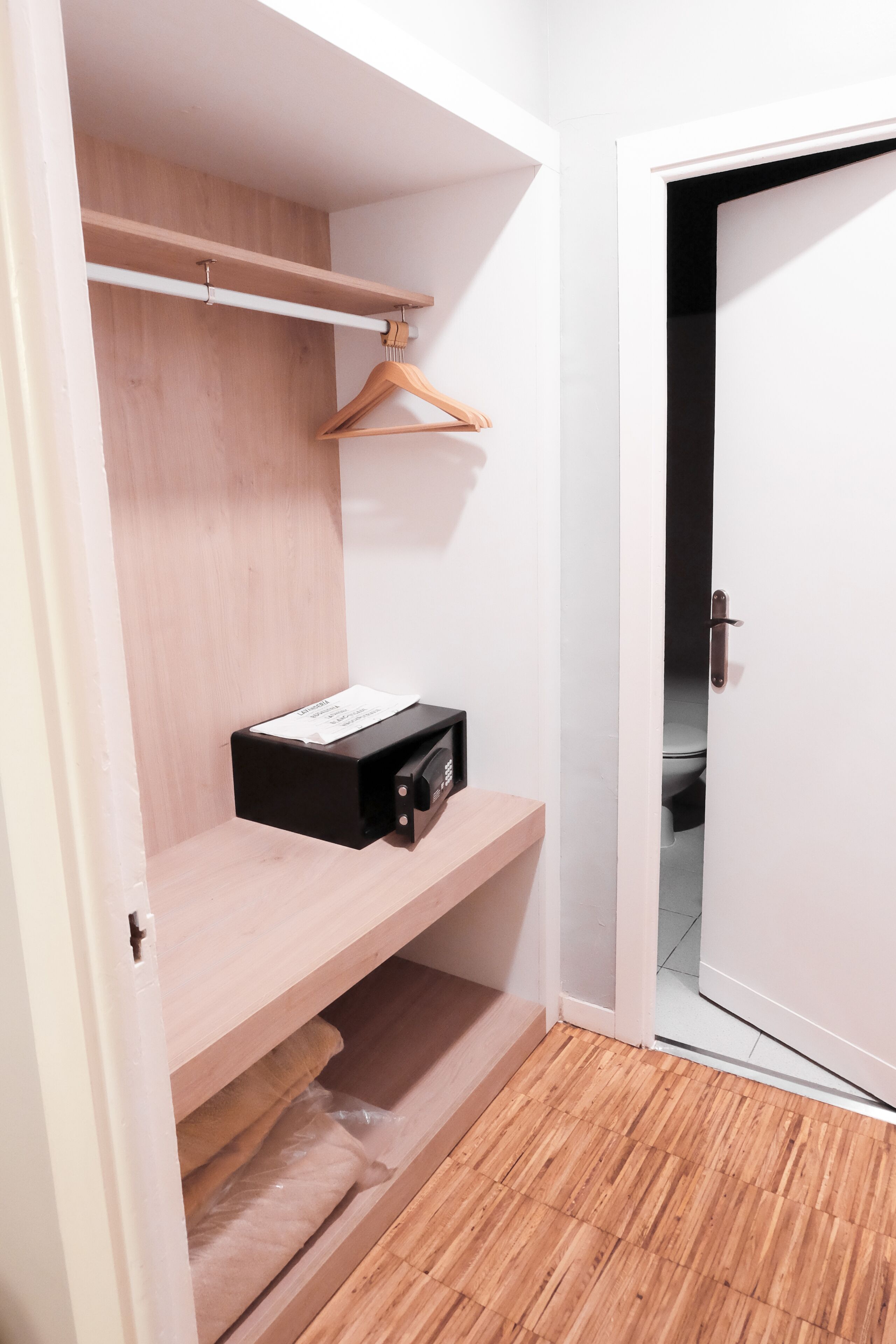 A walk-in closet with wooden shelves, a hanging rack, and a black storage box.