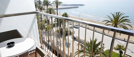 Un balcón con vistas a una playa, palmeras y un edificio lejano.