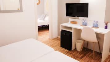 Habitación de hotel con cama, escritorio con computadora, silla, refrigerador pequeño y un basurero.