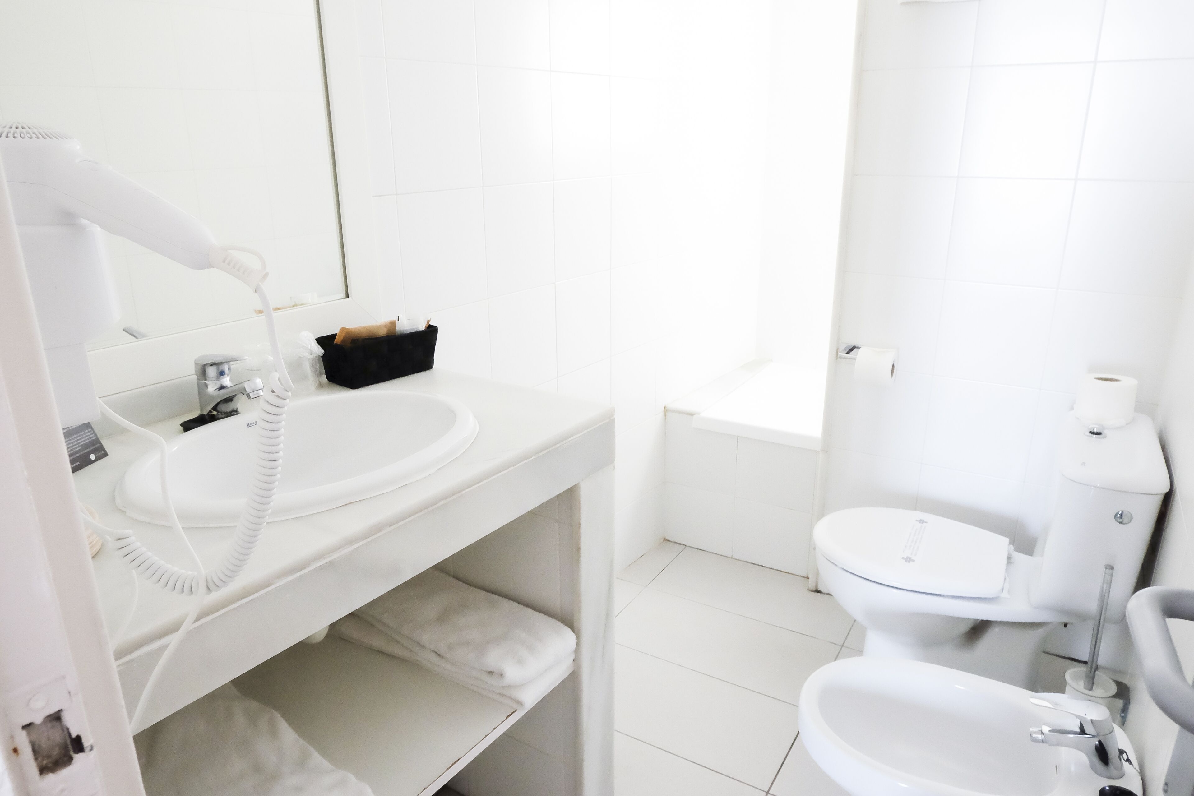 Un baño con lavamanos, espejo e inodoro blancos.