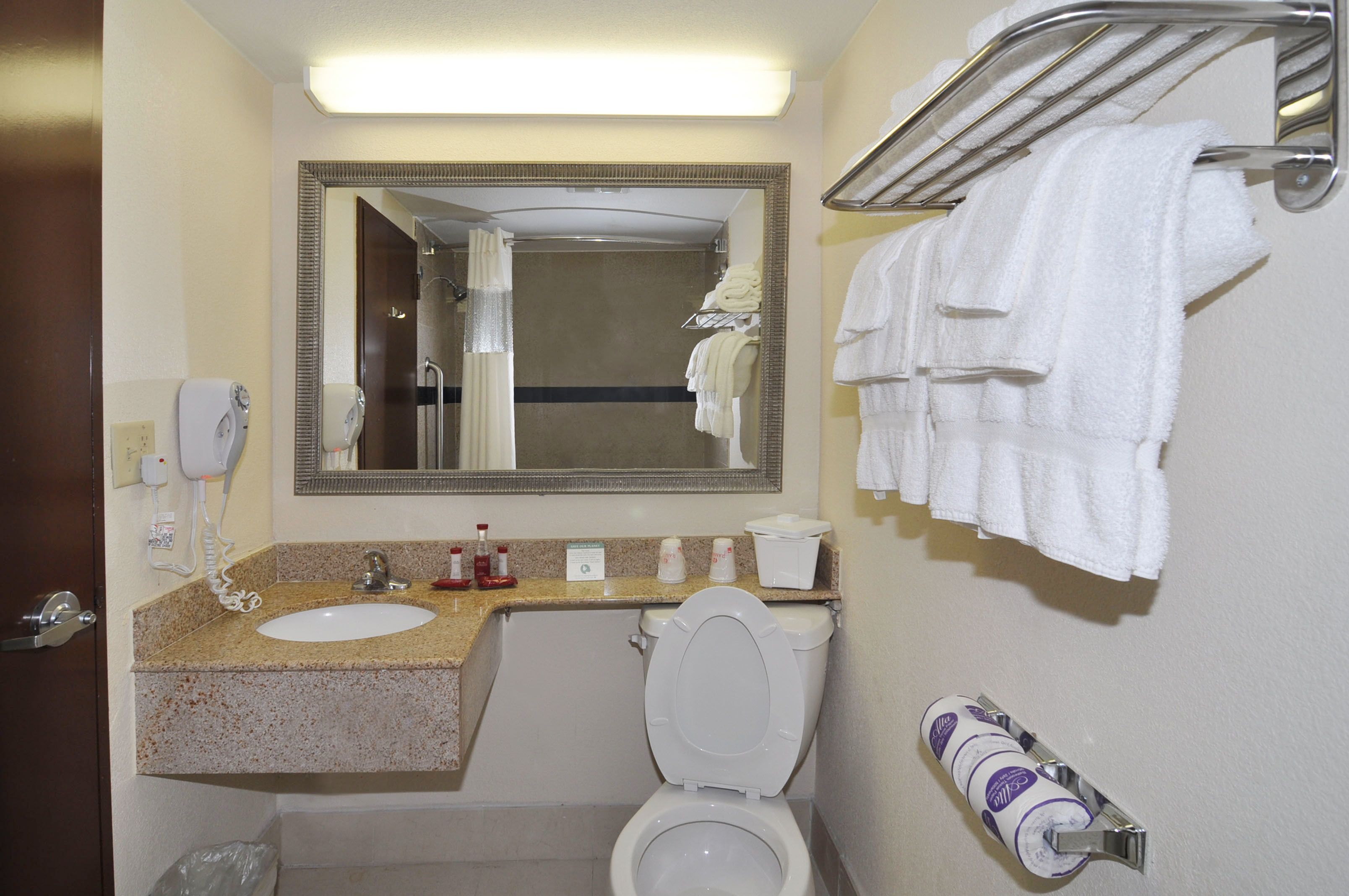 A hotel bathroom with a sink, toilet, mirror, towel rack, and toiletries.