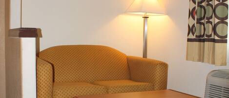 A hotel room with a patterned sofa, a wooden table, a lamp, and a patterned carpet.