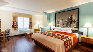A hotel room with a large bed, two bedside tables with lamps, a desk with a chair, a window with curtains, and a cityscape painting on the wall. - Super 8 by Wyndham Beaumont I-10 South/College St (Beaumont)