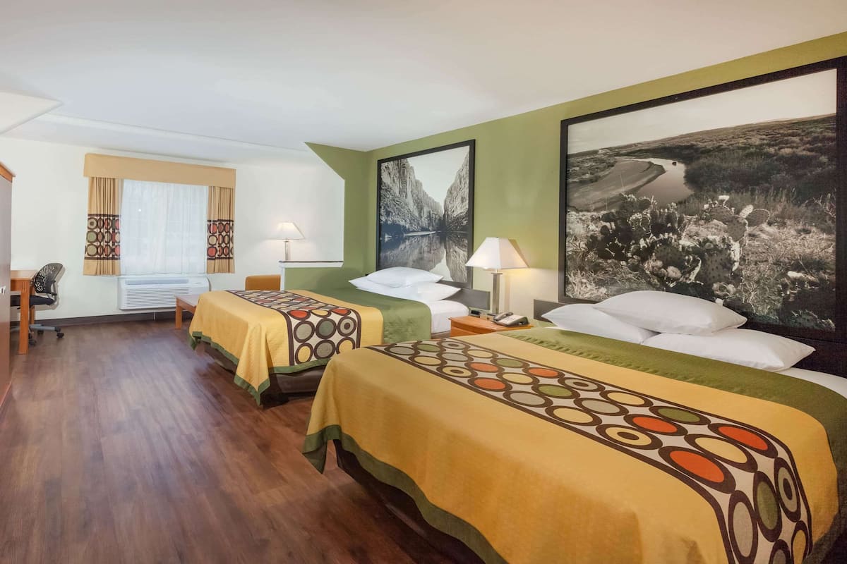 A hotel room with two beds, a desk, and a chair. There are two large framed pictures on the walls.