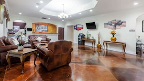 A spacious living room with leather sofas, a wooden coffee table, and a chandelier. - Super 8 by Wyndham Beaumont I-10 South/College St (Beaumont)