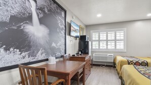 A room with a wooden dining table, chairs, a TV, a heater, and two beds with patterned bedspreads. - Travelers Inn Medford (Medford)