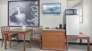 A room with a wooden desk, a television mounted on the wall, a refrigerator, a microwave, and a large framed picture of a landscape. - Travelers Inn Medford (Medford)
