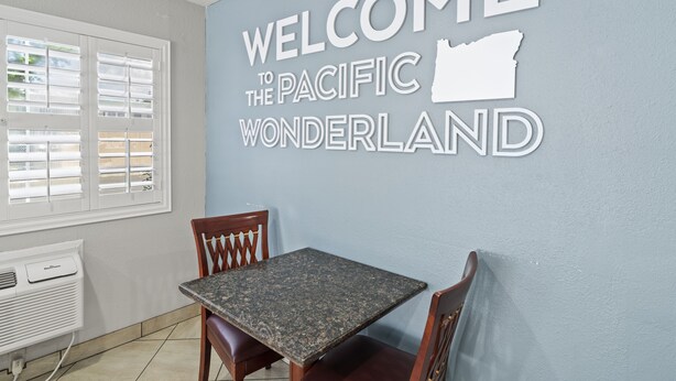 A room with a table and chairs, a window with blinds, and a wall with a welcome sign. - Travelers Inn Medford (Medford)