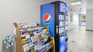 A vending machine with a Pepsi logo, a display of travel magazines, and a wooden rack with various brochures. - Travelers Inn Medford (Medford)