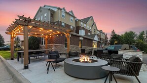 An outdoor patio with a circular fire pit, seating, and a pergola with string lights. - TownePlace Suites by Marriott -Minneapolis West/StLouis Park (St. Louis Park)