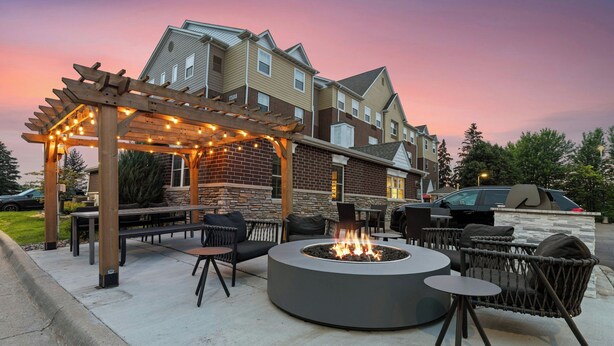 An outdoor patio with a circular fire pit, seating, and a pergola with string lights. - TownePlace Suites by Marriott -Minneapolis West/StLouis Park (St. Louis Park)