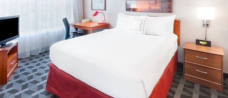Habitación de hotel con una cama grande, un escritorio con lámpara, un televisor y una mesita de noche con lámpara.