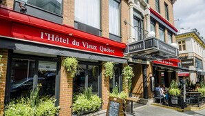 L’extérieur de l’« Hôtel du Vieux-Québec », avec son auvent rouge, sa façade en briques et son espace extérieur aménagé avec des plantes.