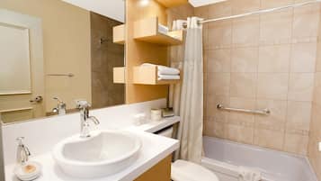 A modern bathroom with a large sink, toilet, and bathtub. There are wooden shelves with towels and toiletries.